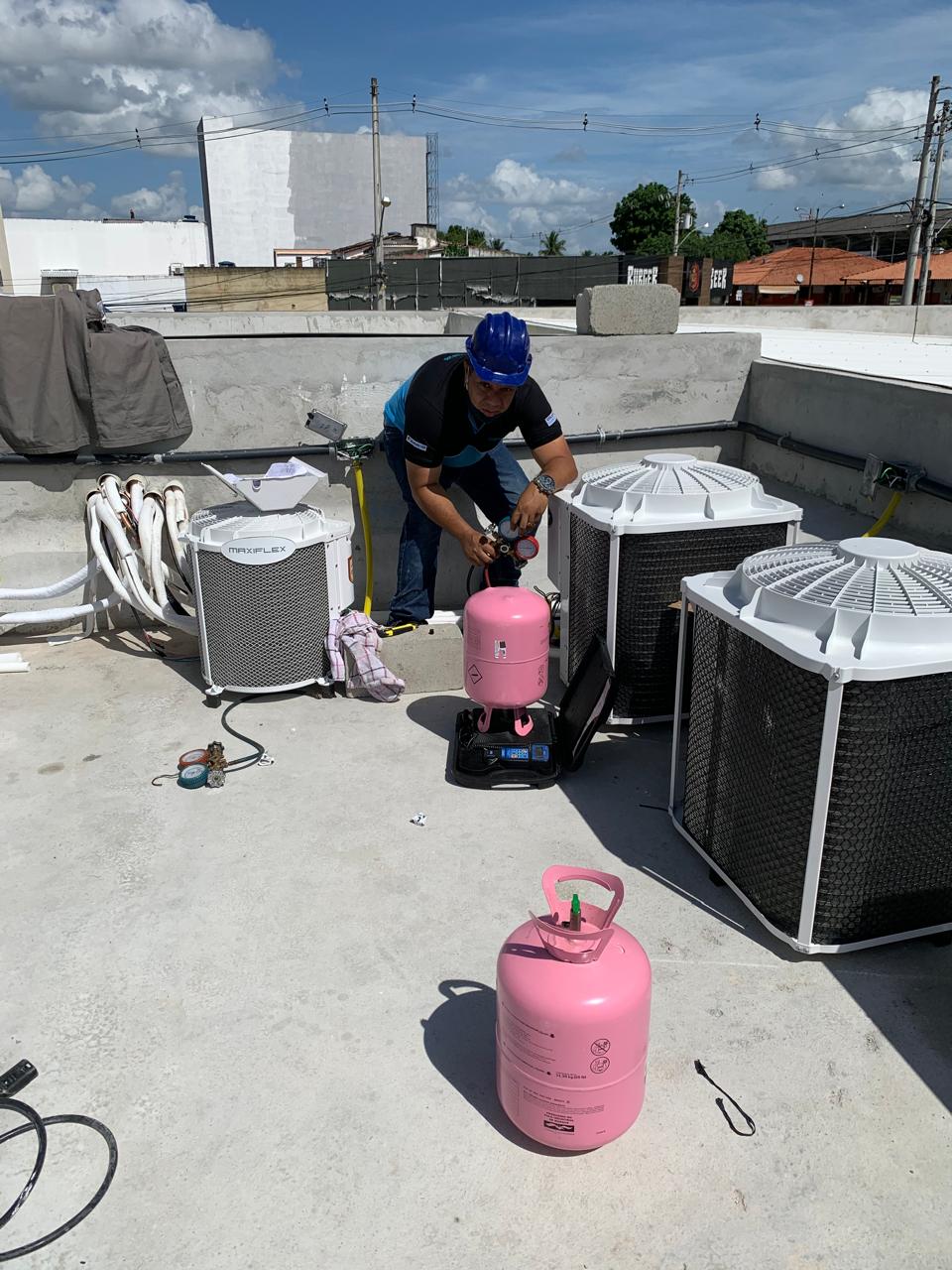 Técnico com capacete fazendo carga de gás refrigerante em condensadoras na laje