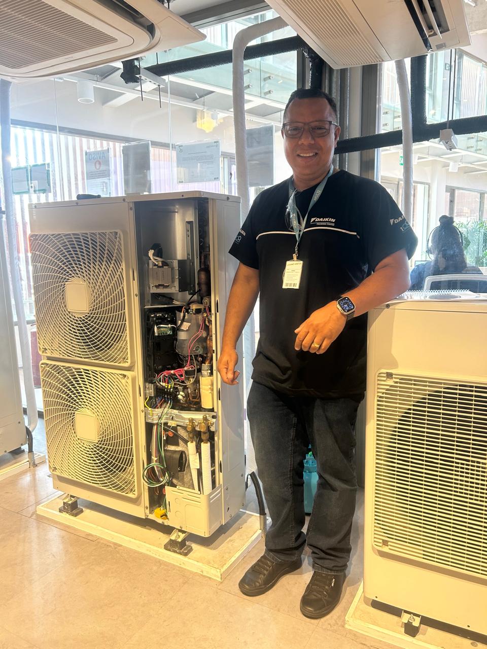 Técnico da Forte Refrigeração sorrindo ao lado de equipamento de ar-condicionado VRF